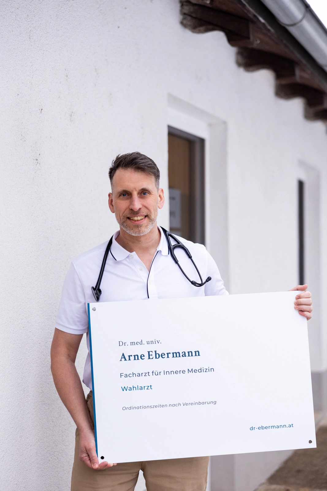 Dr. Arne Ebermann vor der Ordination mit Ordinationsschild in der Hand